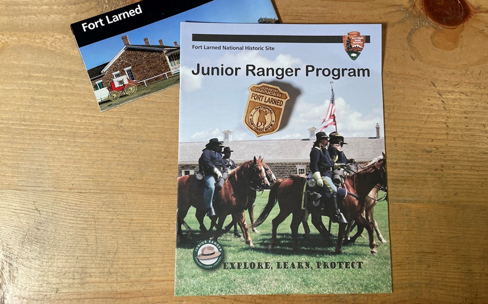 Junior Ranger book on wooden counter. Badge sits on top of book with park brochure above it.