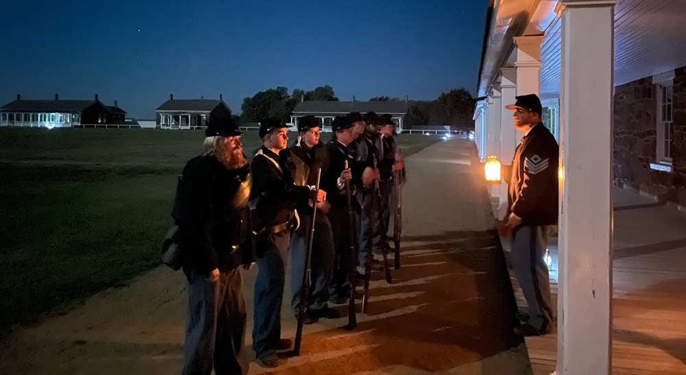 Several soldiers are lined up in front of the barracks at night.