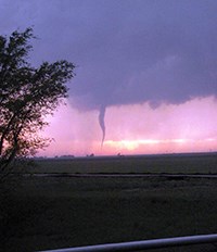 Evening view of prairie landscape with a tornado in the distance.