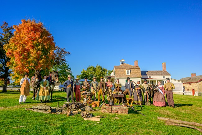 Living historians in 1800s clothing gathered in farm yard with houses in background