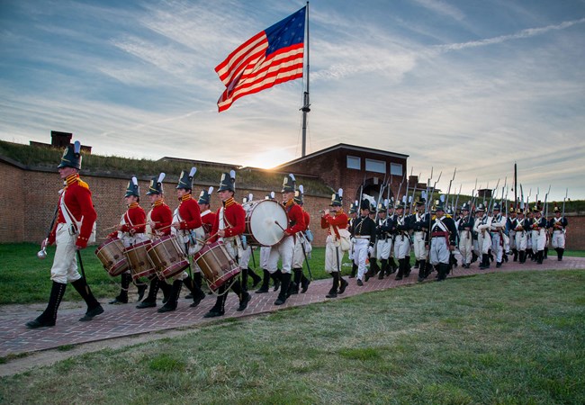 Living history volunteers march outside of star fort  in War of 1812 uniforms