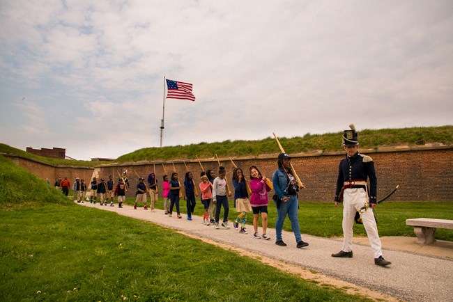 Students marching outside fort with wooden muskets