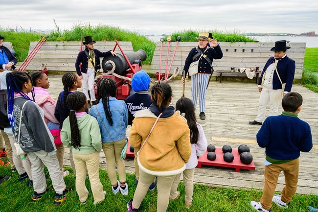 Students observing living history members on historic weapons deck.