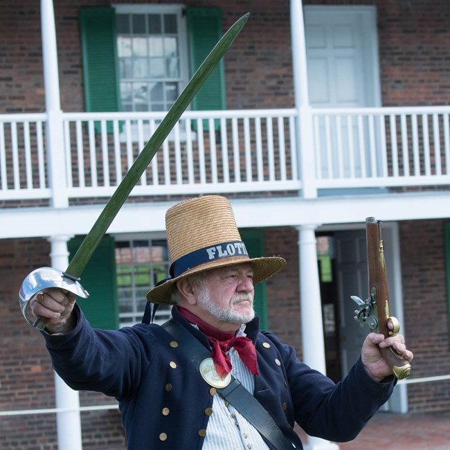 A living historian dressed as flotilla sailor holds up a pistol and sabor