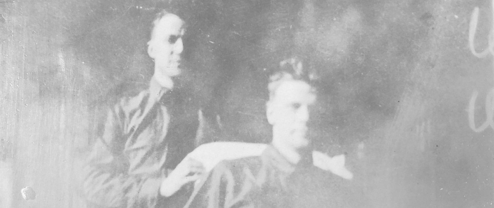 A historic black and white photograph showing two men, one sitting.