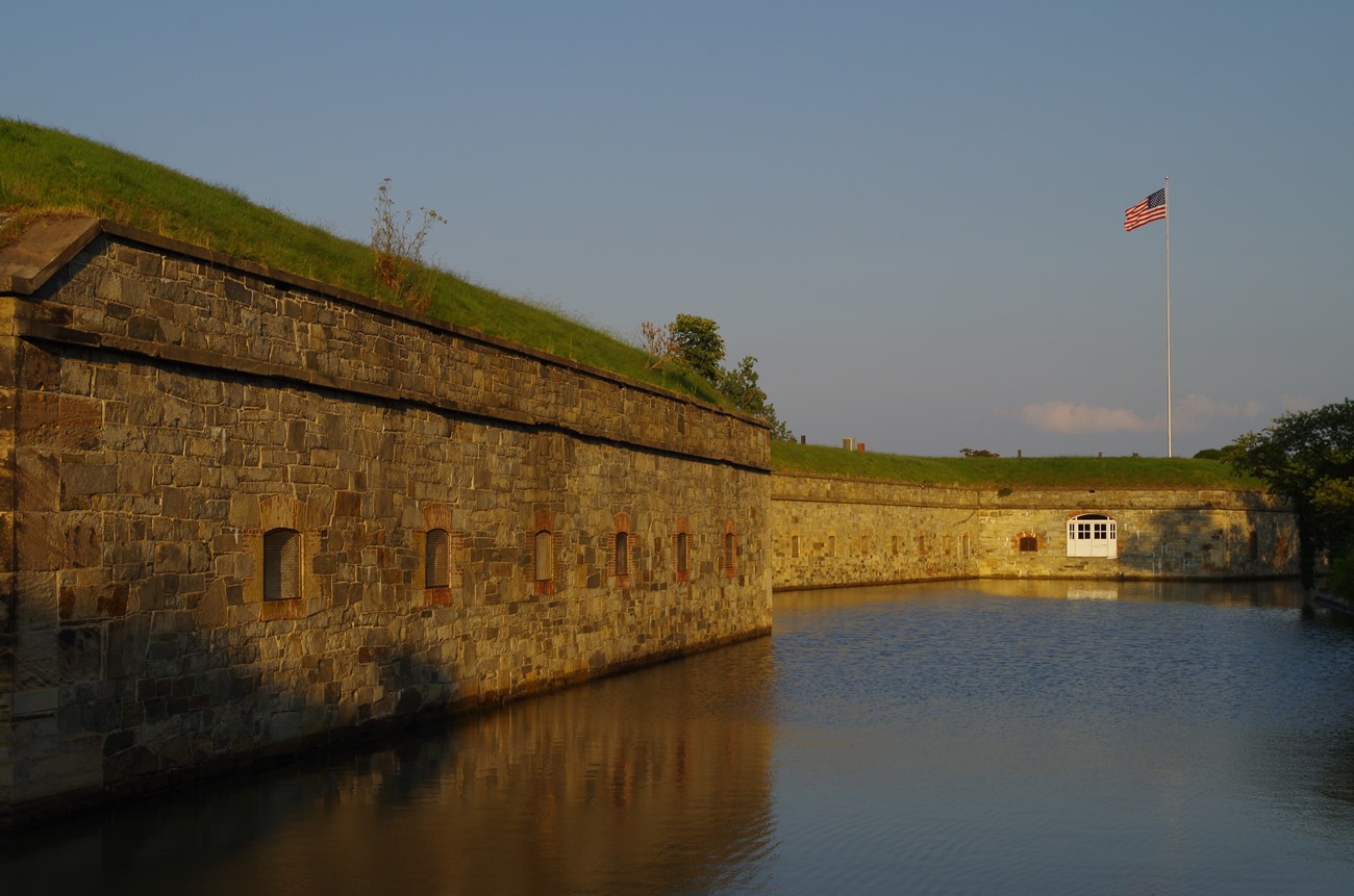 The setting sun lights a stone fort wall where a US flag flies high.