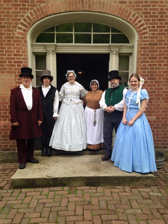 A group of volunteers in historic dress stand in the doorway to the Mount Washington Tavern