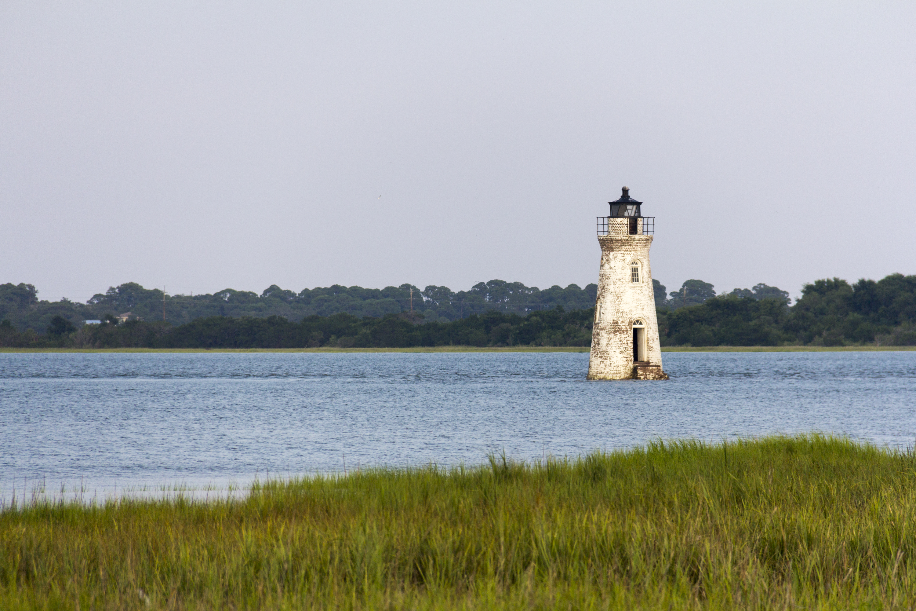 White lighthouse surrounded by water with marsh in the foreground.