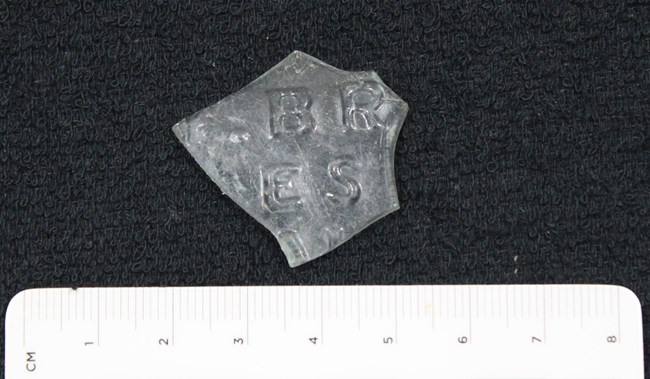 Colorless glass fragment with a few letters embossed on the side