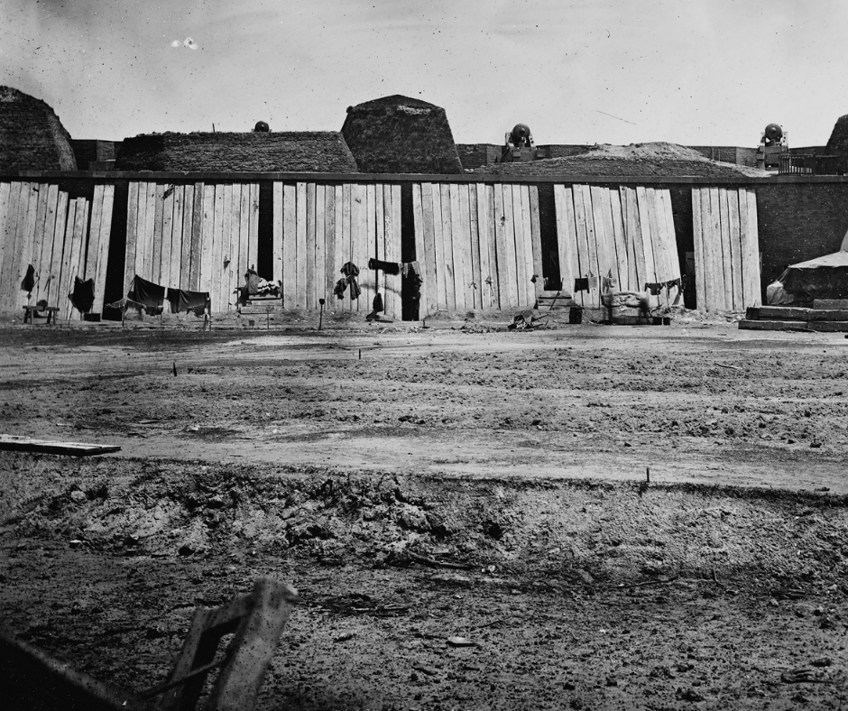 Black and white photograph of the inside of Fort Pulaski after the bombardment. Wooden slats, or blindage, protect the casemates and three cannons are on the upper level.