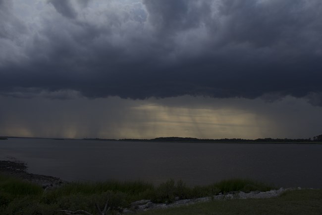 Storm clouds and rain over a wide river.