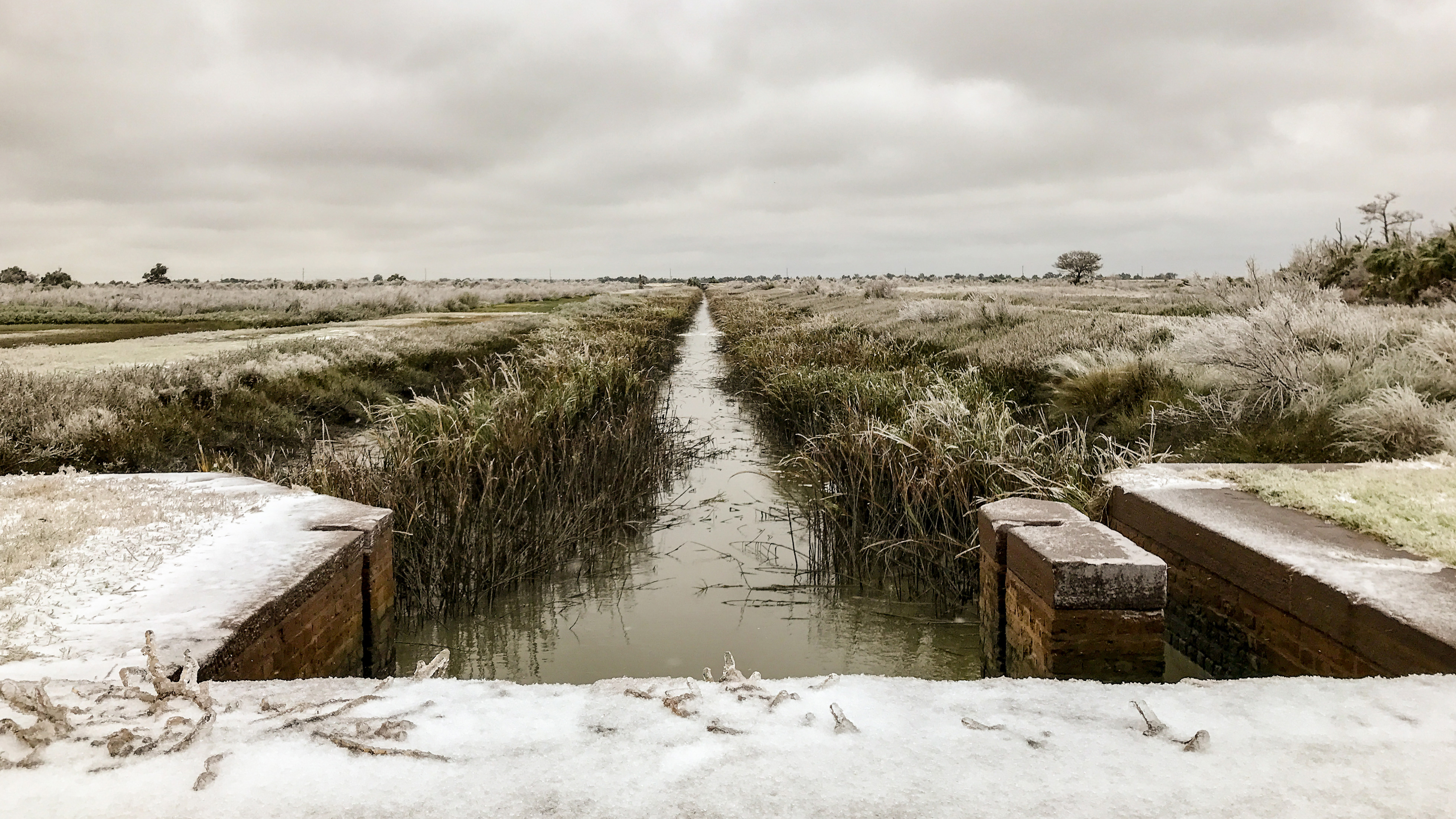 Ice and snow cover the sandstone ruins of a water gate and marsh grass that surrounds a canal of water are heavy with ice.
