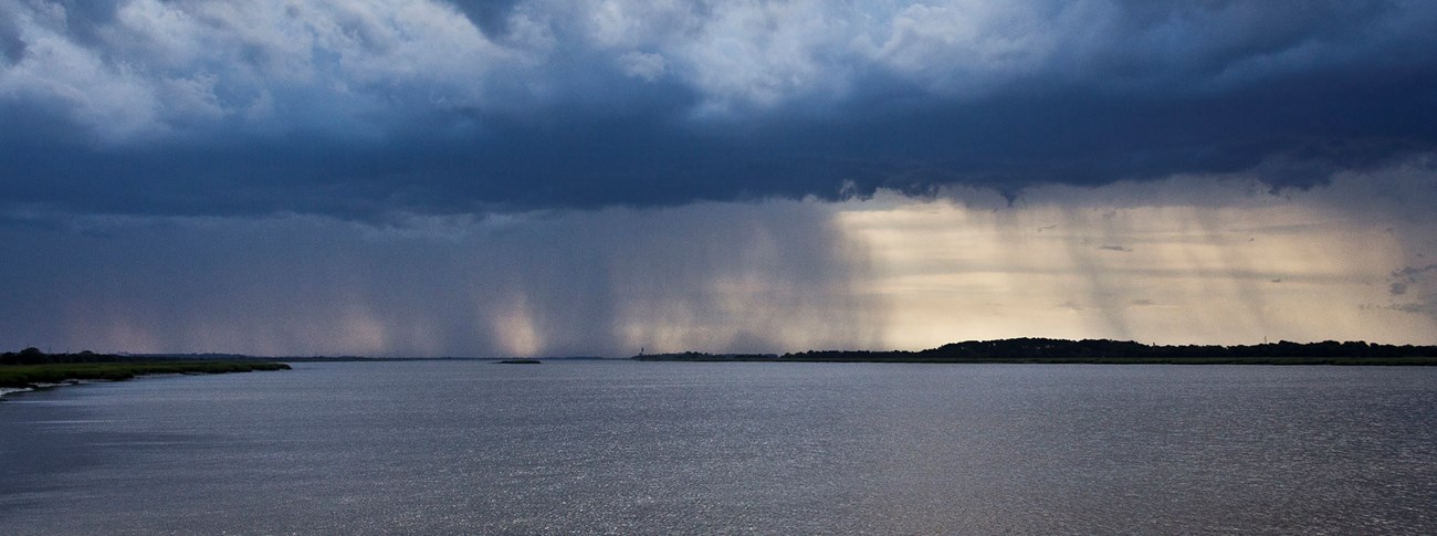 A photograph of storm clouds and rain approaching Cockspur Island from Savannah, Georgia.