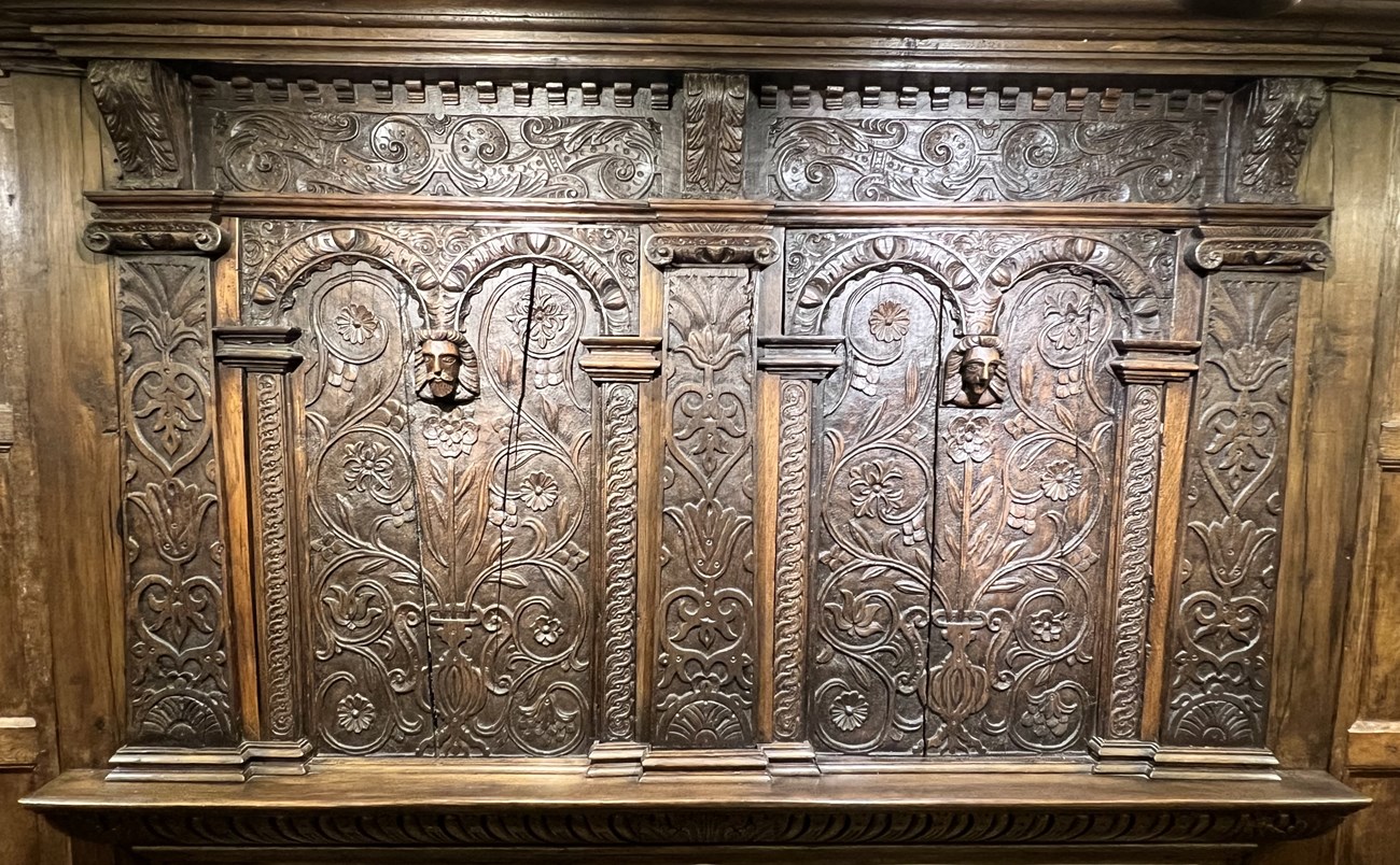 Dark wood panel with ornate carvings above fireplace mantle