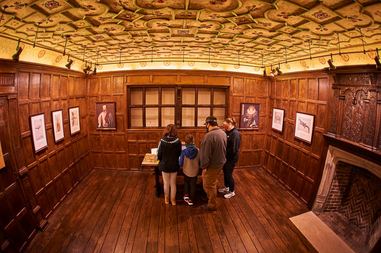 Oak paneled room with plaster ceiling. Family reads exhibit.