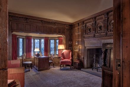 Okay paneled study with red furniture and large fireplace.