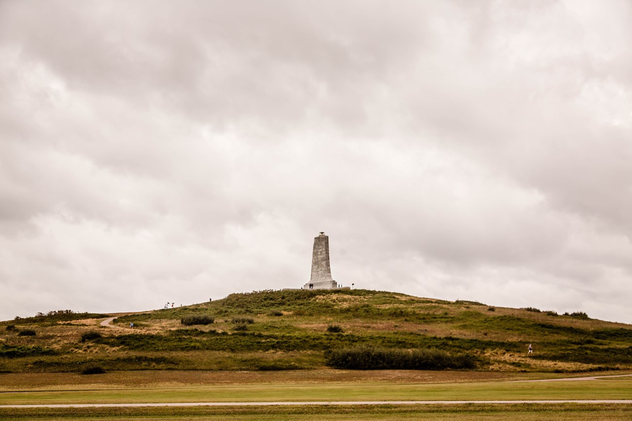 Visitors walking up paths on a tall grassy hill leading to a granite monument at the top