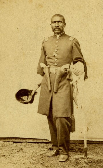 Civil War Era photo of William Mathews, a Black captain, in uniform with two revolvers on his belt and holding a saber.