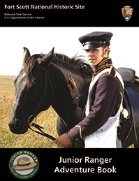 Young man in an 1840s solders field uniform holding the reigns of a black horse.