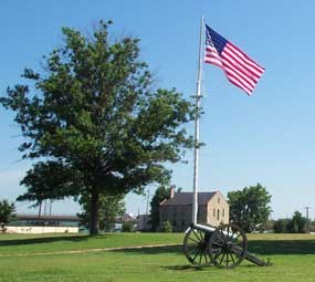 Garrison flag flies in middle of parade ground with commissary in distance
