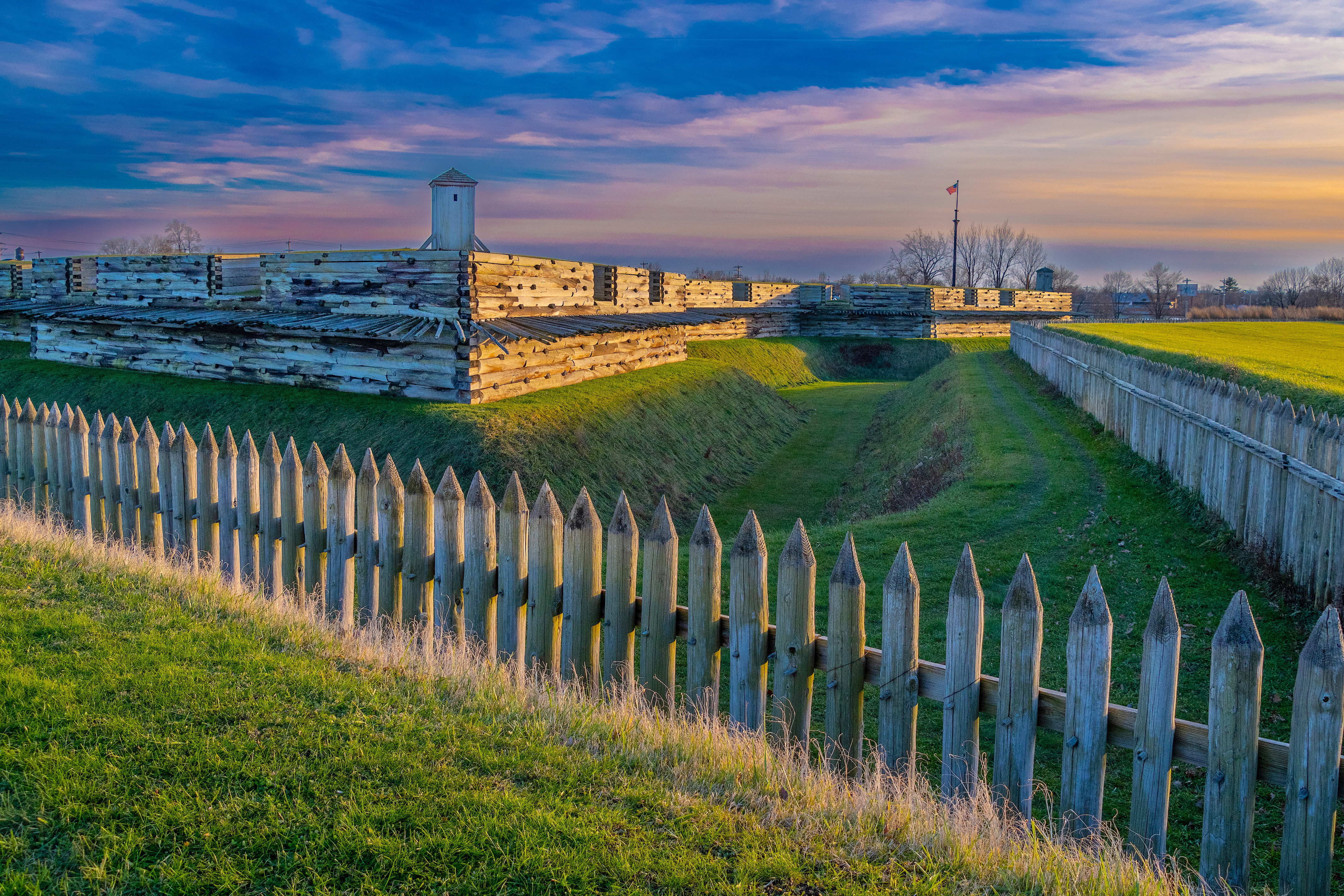 Looking at the fort wall from an outside corner, pastel colors paint the sky and highlight the wooden walls with light.