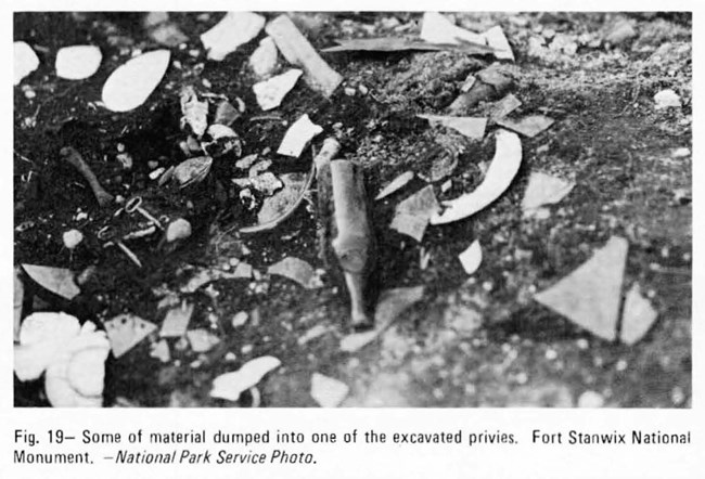 A black and white picture of various bits of glass and pottery shards in a dirt hole.