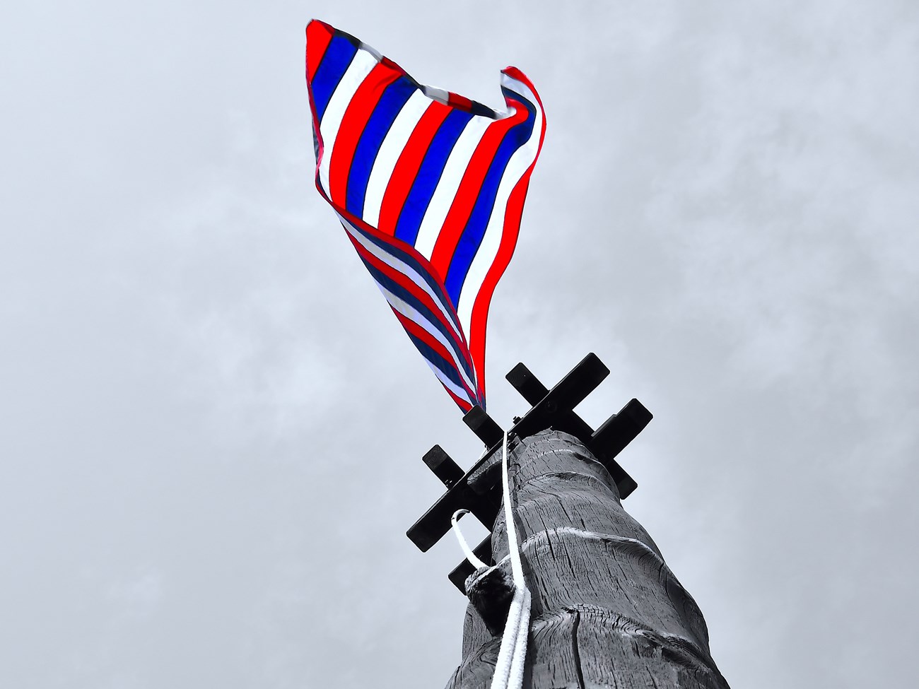 Looking up a wooden ship's mast-like pole, a pop of color and a red, white, and blue flag flutters at the top, over your head.