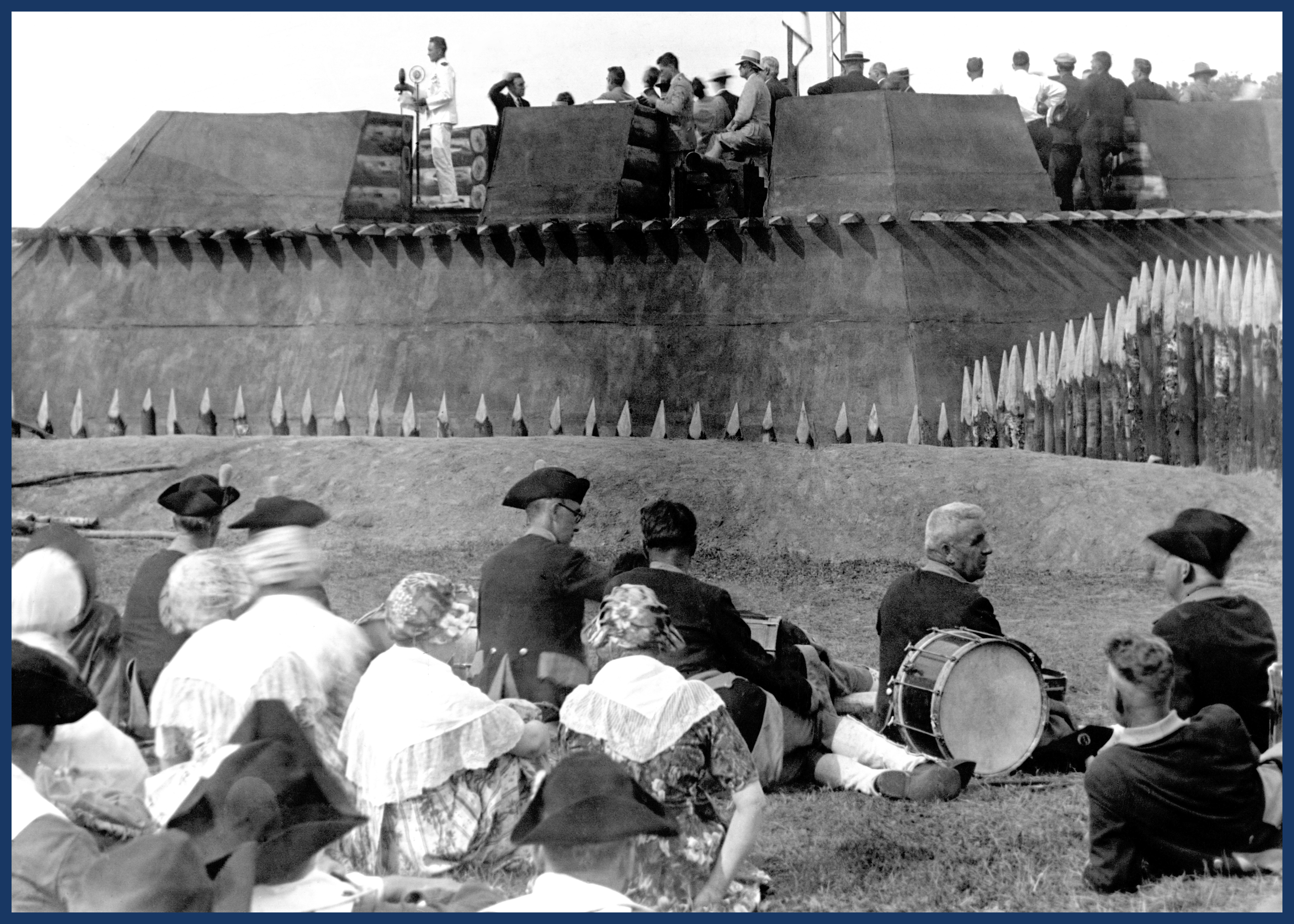 An airforce colonel stands in a reconstructed bastion and addresses a crowd, some of whom are dressed in 18th century period clothing.