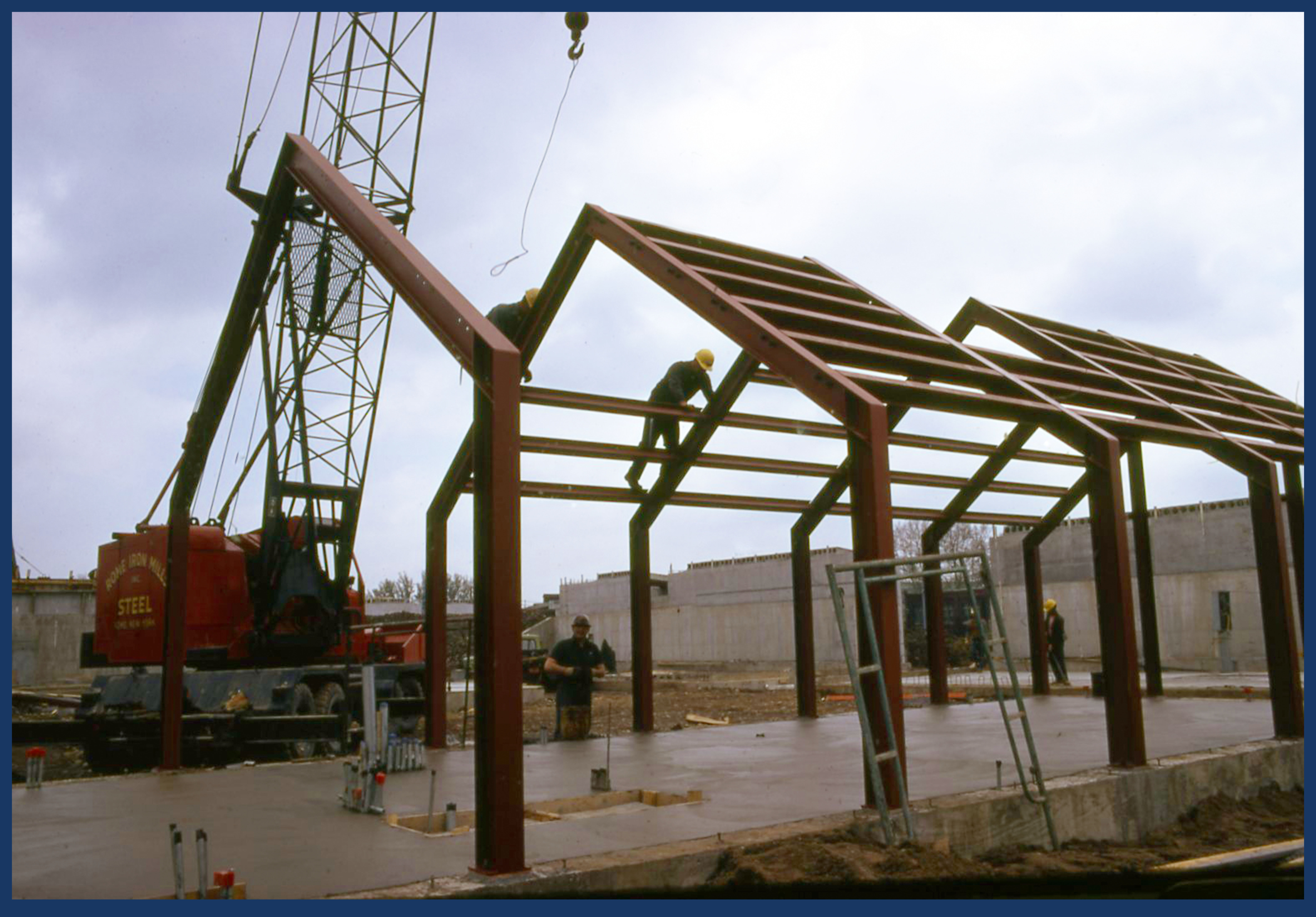 A large steel frame anchored in concrete sits on the parade ground of Fort Stanwix with a crane in the background.