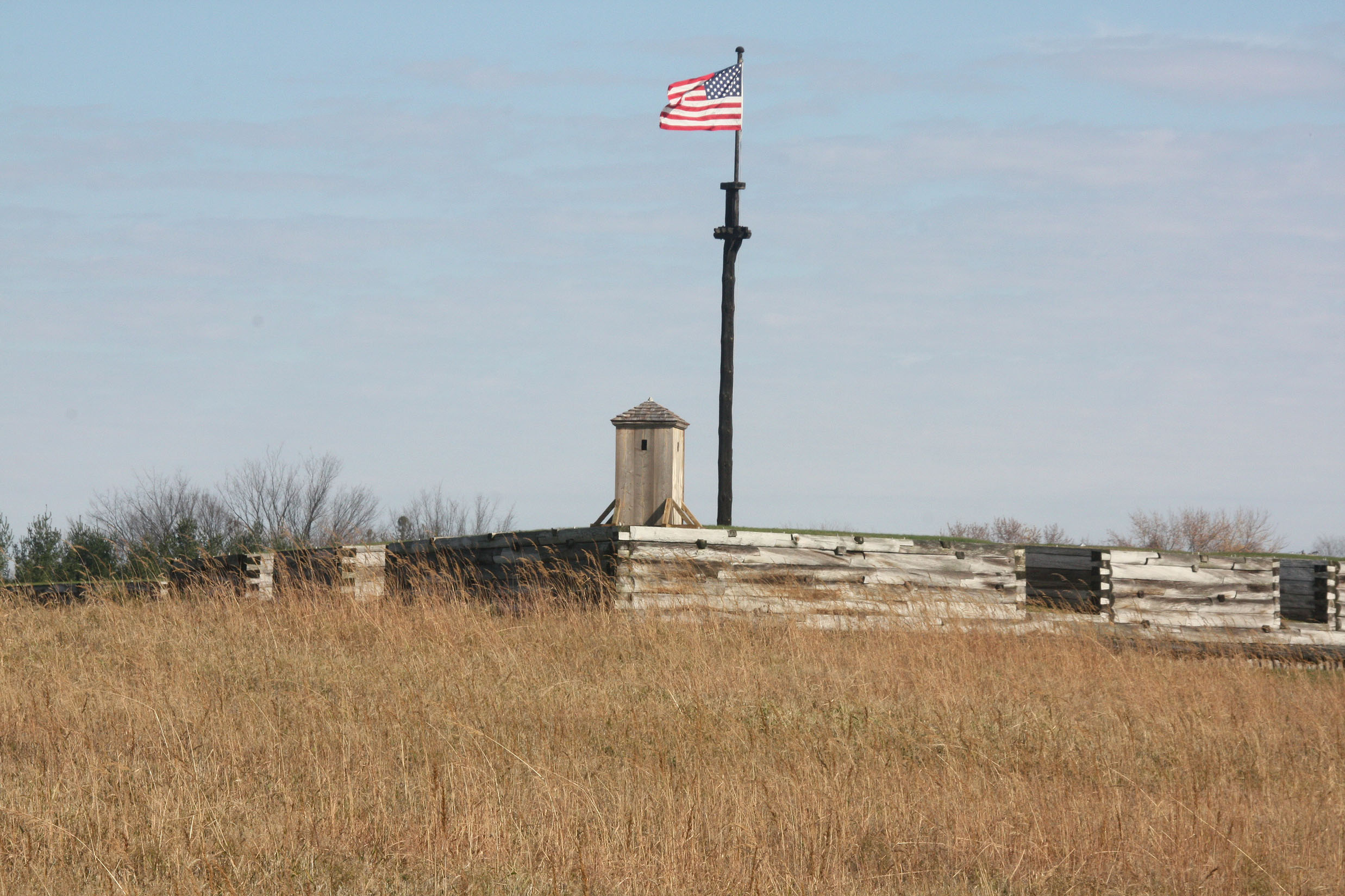 An American flag flies from a large flag mast over the wood walls of the fort.