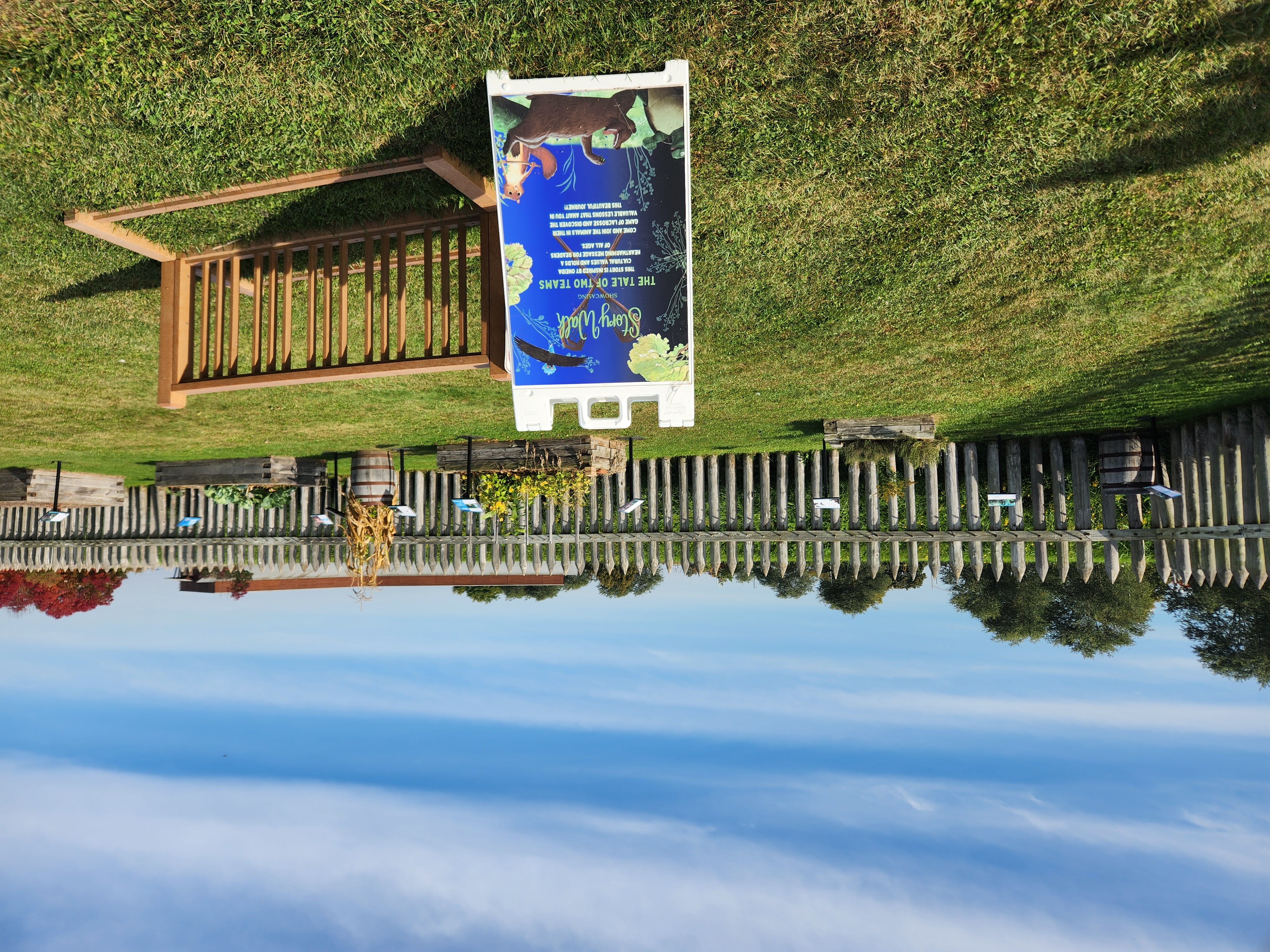 A bright day, with puffy clouds floating overhead. In front of you, colorful sign boards and a lush garden with wooden pickets behind.