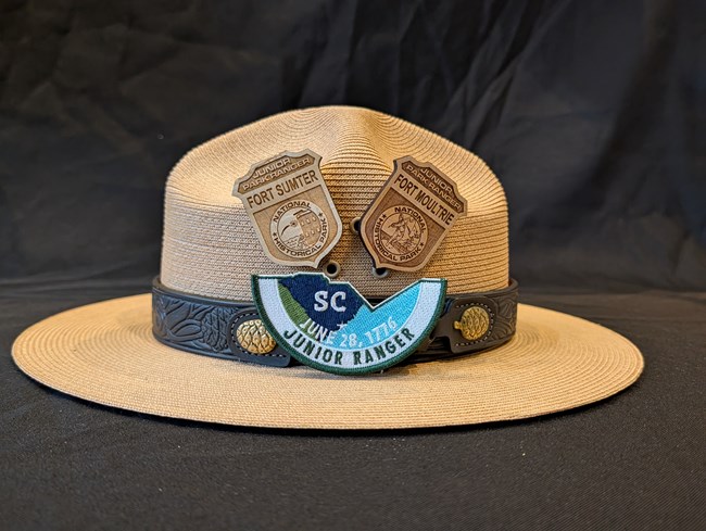 Fort Sumter and Fort Moultrie Junior Ranger Badges on a ranger hat