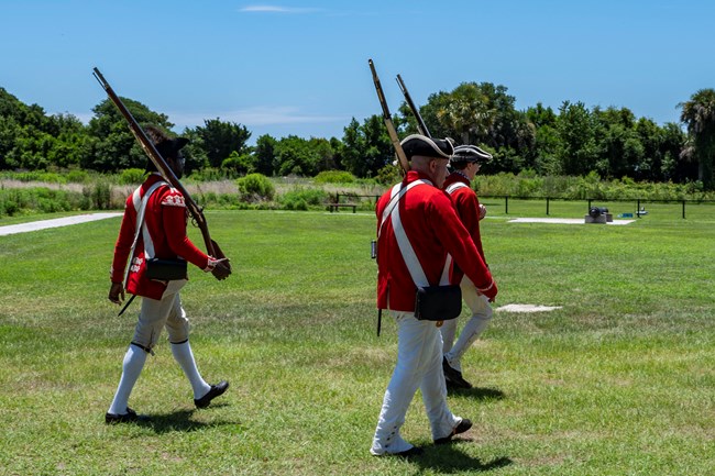 Living historians dressed as British soldiers cross a field