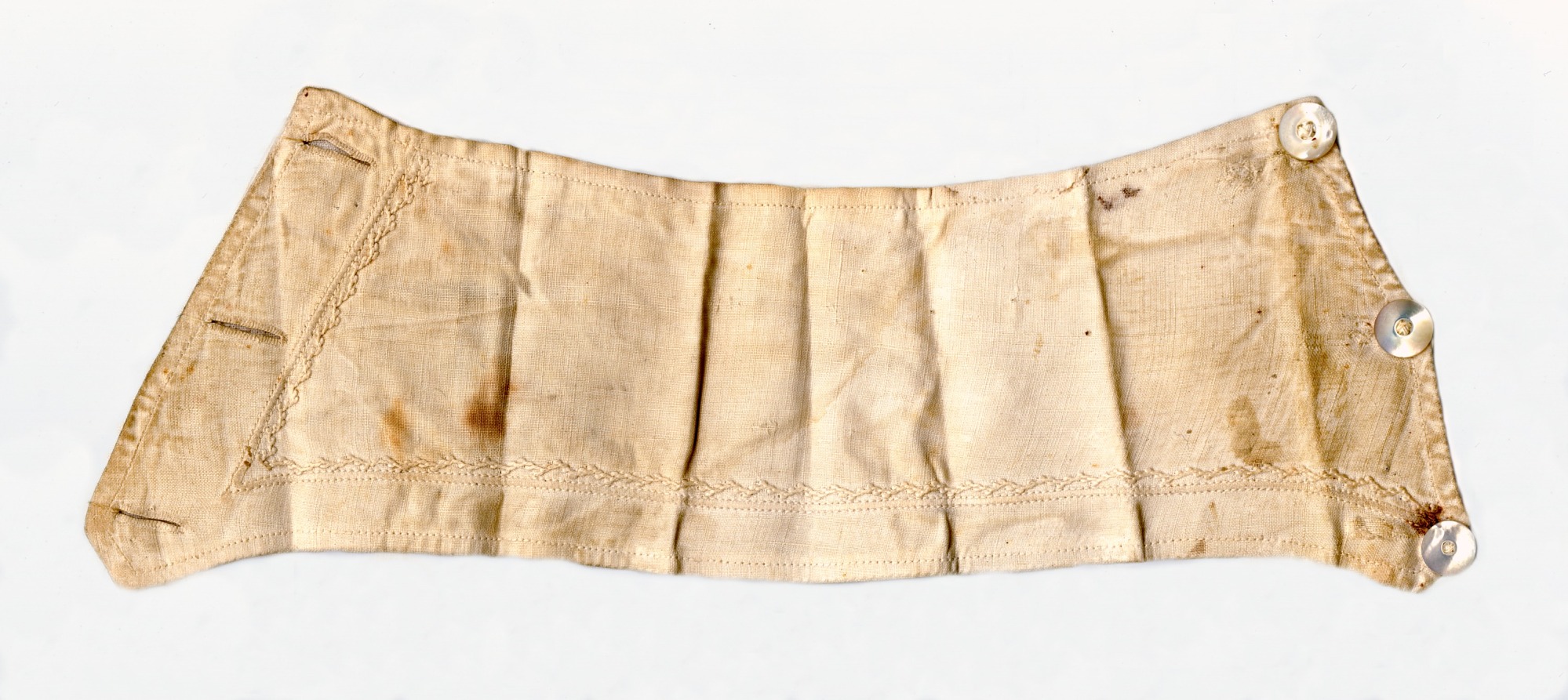 Off white sleeve cuff with an embroidered pattern, three buttonholes on one side, and three pearl buttons on the opposite side, with folding creases and dark red-brown stains