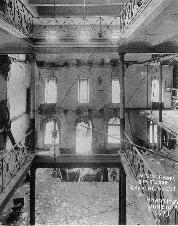 black and white photo showing three story building where the floors have partially collapsed about half way. The view looking towards the front of the building showing the doors and windows. On the photo is written view from second floor looking west, Bra