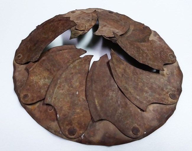 circular metallic object with metallic leaves that fold inward in overlapping fashion around circumference of object