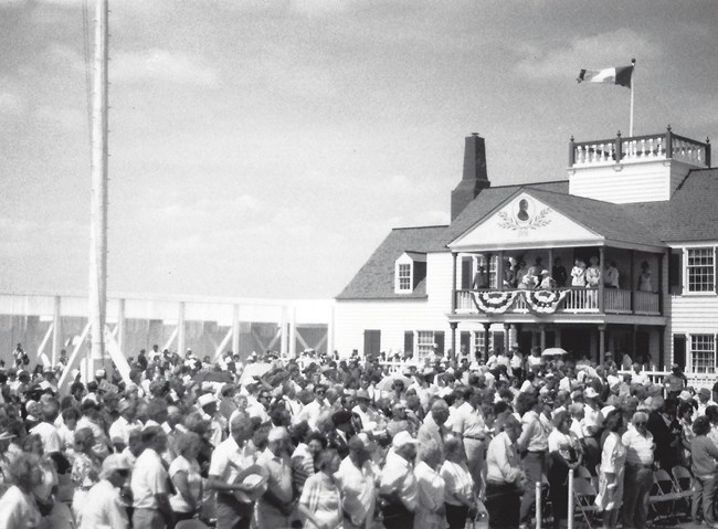 Large crowd of people standing in front of a white house.