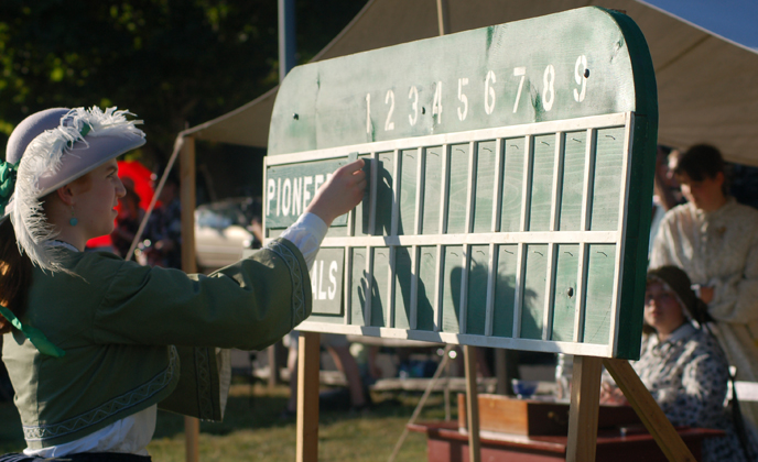 Image of costumed woman adjusting the scoreboard at an 1860s vintage base ball game.