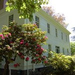 Photo of the exterior of the McLoughlin House with a red rhodedendron in the foreground.