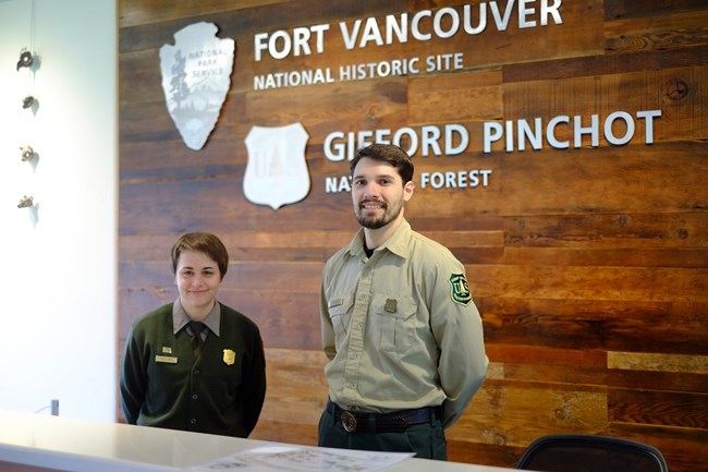 A national park ranger and a forest ranger stand together inside the Fort Vancouver Visitor Center