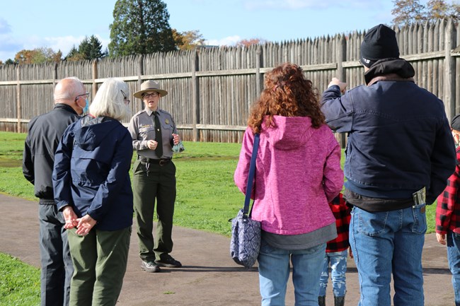 Park Ranger leads visitors on paved path in front of large white, square Counting House.