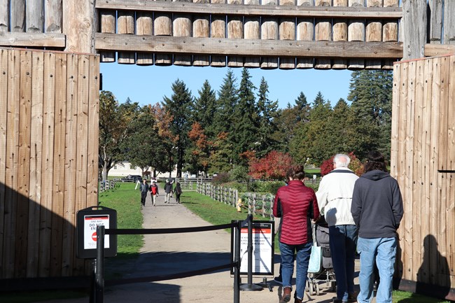 Group of adult visitors clustered at the front gate of the fort, framed by the tall wooden gate and fort walls.