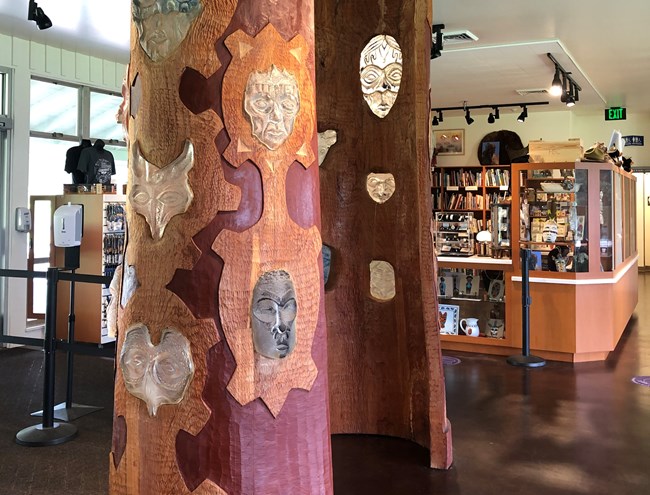 Visitor Center interior with large wooden spirit pole mounted vertically inside building. Pole has glass inclusions shaped as animal masks.
