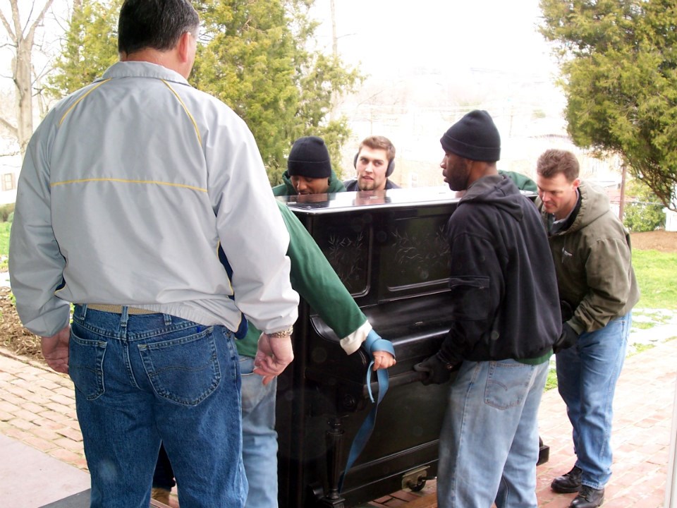 A crew carries an old upright piano