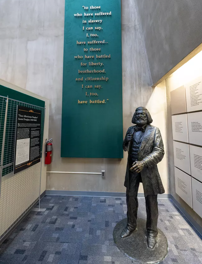 A statue of Fredrick Douglass stands next to the quote, "To those who have suffered in slavery I can say, I, too have suffered... to those who have battled for liberty, brotherhood, and citizenship I can say, I, too have battled."
