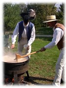 Two men stirring a steaming kettle over a fire