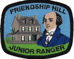 Blue patch with black border.  The words "Friendship Hill Junior Ranger" are embroidered above and below the embroidered images of the Stone house and bust of Albert Gallatin