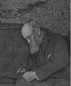 Black and white of elderly man in suit with gray beard bent over and writing something