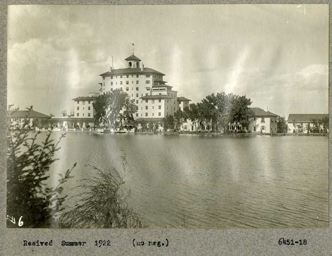 Black and white of large body of water, with large building on the edge across, with some trees scattered.