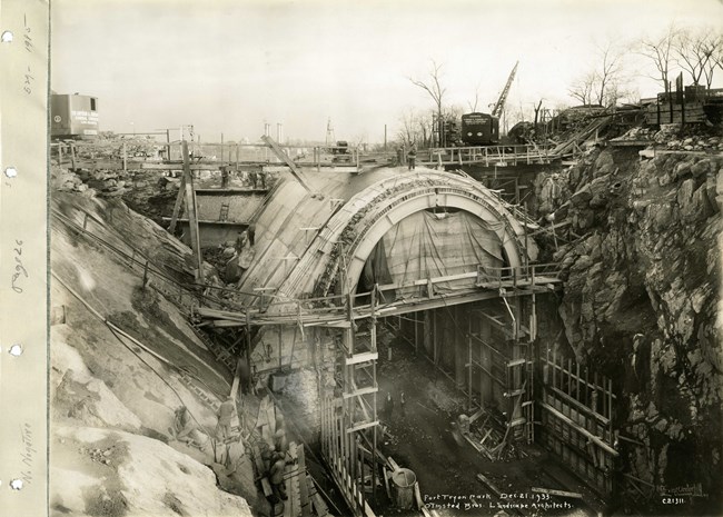 Black and white photograph of arch being built between two rock walls, with wooden planks extending from both sides.